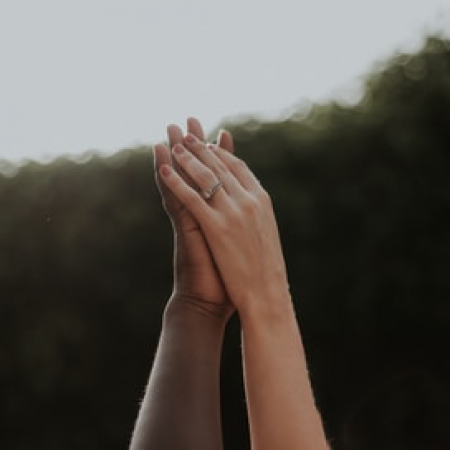 Two raised hands pressed together with wedding rings